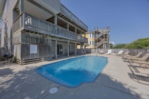 A pool area with a wooden deck, lounge chairs, and a multi-story building with balconies. - 1818 - It's A Shore Thing, 70 Yards to Beach | Pool, Hot Tub & Elevator (Corolla)