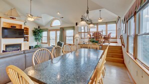 A spacious kitchen with a granite countertop, wooden chairs, and a dining table. There are ceiling fans, large windows, and a view of the city. - 1818 - It's A Shore Thing, 70 Yards to Beach | Pool, Hot Tub & Elevator (Corolla)