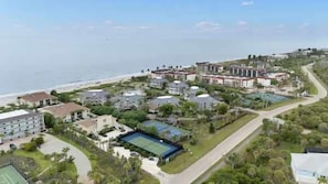 A coastal hotel complex with multiple buildings, a tennis court, and a beach view. - Villa Sanibel 1C |  Premier Beachfront Residence on Sanibel Island (Sanibel)
