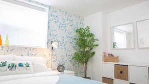 A bedroom with a bed, a nightstand, a wall clock, a potted plant, and a white cabinet with storage boxes.