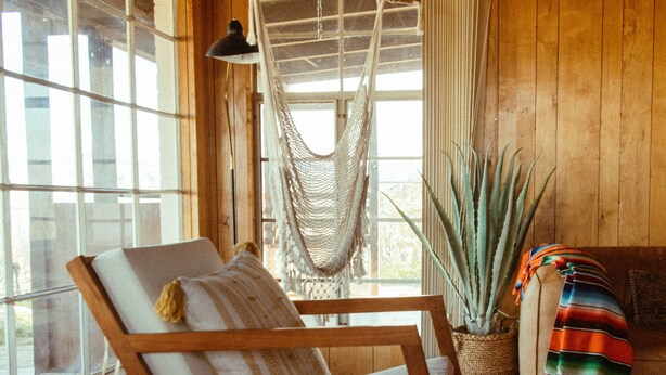 A wooden interior with a rocking chair, a hammock, and a potted plant.