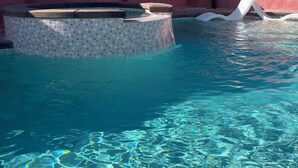 A clear pool with a tiled edge, a hot tub, and a pink wall in the background.