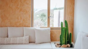 A room with a white sofa, a window with a view of a desert landscape, and a cactus plant.