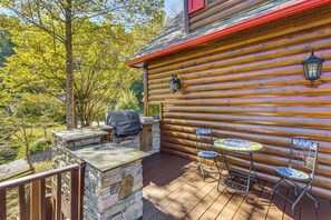 Een houten chalet met een stenen open haard, een barbecue en twee stoelen.