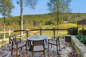 Een terras met een ronde tafel en vier stoelen, met uitzicht op een schilderachtig meer en beboste heuvels.