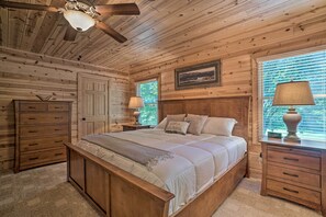 Een slaapkamer met houten lambrisering, een bed, nachtkastjes, een dressoir en een plafondventilator.