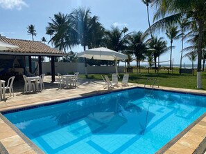 En pool med solstolar och parasoller, omgiven av palmer och med utsikt över havet.