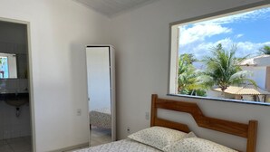 Ein Schlafzimmer mit einem Bett, einem Fenster mit Blick auf Palmen und einem Badezimmer mit Waschbecken und Spiegel.