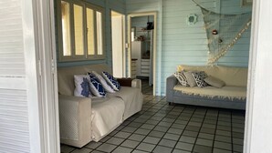 Ein Zimmer mit Fliesenboden, einem beige gefärbten Sofa mit gemusterten Kissen, einem blauen Sofa und einer Netzdekoration.