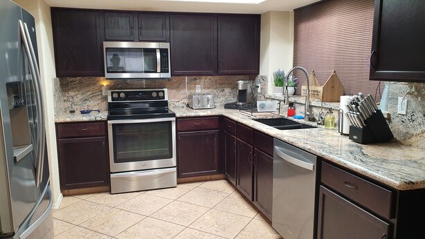 A kitchen with dark wooden cabinets, stainless steel appliances including a microwave, oven, and dishwasher, a granite countertop, and a sink with a knife block.