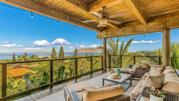 A covered outdoor seating area with wicker furniture, a ceiling fan, and a view of the ocean and mountains. - Spectacular Panoramic Ocean Views - Private Ohana - Wailea Custom Pole Home (Kihei)