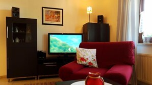 Una sala de estar con un sofá rojo, un televisor, un aparador y una mesita con una maceta roja.