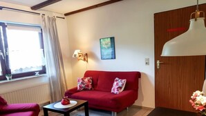 Una habitación acogedora con un sofá rojo, una mesita con un objeto rojo, una lámpara y un cuadro en la pared.