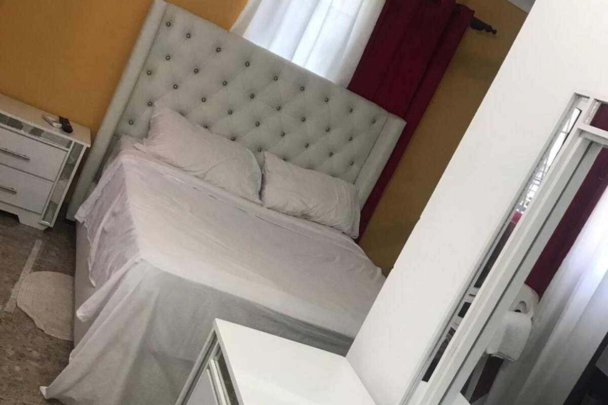 Un dormitorio con una cama de cabecera capitonada, una mesita de noche, un armario y un espejo.