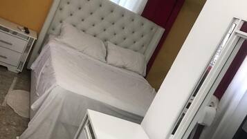 Un dormitorio con una cama de cabecera capitonada, una mesita de noche, un armario y un espejo.