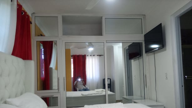 Una habitación de hotel con cama, televisor montado en la pared y un espejo que refleja el cuarto.