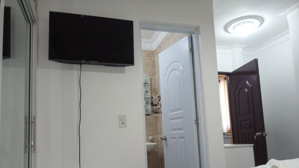 A bedroom with a bed, a TV mounted on the wall, a bedside table, and a door leading to another room. - Estudio Vegano (La Vega)