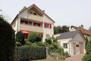 Un bâtiment à deux étages doté d’un balcon, d’une petite dépendance attenante et d’un parasol rouge.