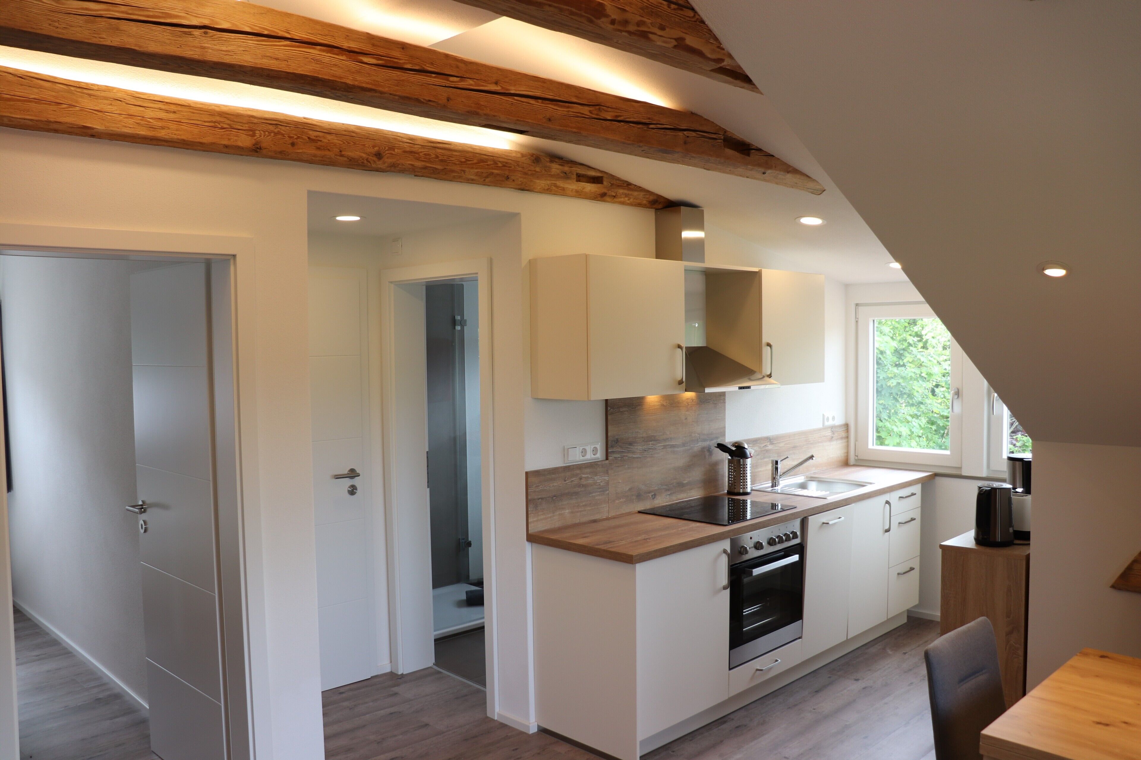 Eine moderne Küche mit Holzbalken, weißen Schränken und einem großen Fenster.