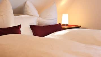 Ein ordentlich bezogenes Bett mit weißen und dunkelroten Kissen, eine Nachttischlampe und ein Holfnachtkästchen.