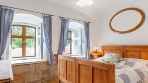 A bedroom with a wooden bed, a stone wall, and a large window with curtains. - Dolní Olešnice by Interhome (Hostinne)