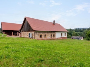 Une grange rustique avec un toit rouge et des murs en pierre, entourée d’un champ verdoyant.