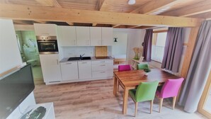 Cocina compacta con armarios blancos, una mesa de comedor de madera y sillas coloridas.