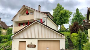 Un edificio de dos pisos con fachada color beige, una puerta roja y un letrero que dice 'Lus Angela Ferienwohnungen'.