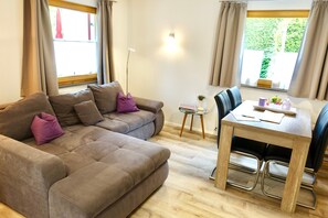 A modern living room with a sectional sofa, a dining table with chairs, and large windows with curtains.