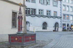 A cobblestone street with a red and gold decorative structure in the foreground and a white building with arched windows in the background.