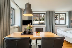 A modern dining area with a wooden table, black chairs, a pendant light, and a TV on the wall.