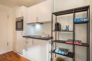 A modern kitchen with white cabinets, a built-in oven, a coffee machine, and a bookshelf with books.