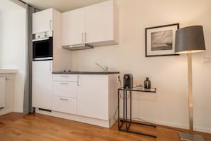 A modern kitchen with white cabinets, a built-in oven, a sink, and a floor lamp. - Modern Studio Apartment No. 14 in the City Center with Wi-Fi (Wangen im Allgäu)