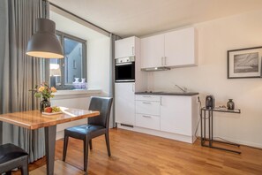 A modern kitchen with white cabinets, a built-in oven, and a dining area with a table and chairs. - Modern Studio Apartment No. 14 in the City Center with Wi-Fi (Wangen im Allgäu)