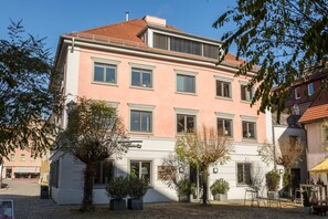 A multi-story building with a pink facade, multiple windows, and a courtyard with potted plants.
