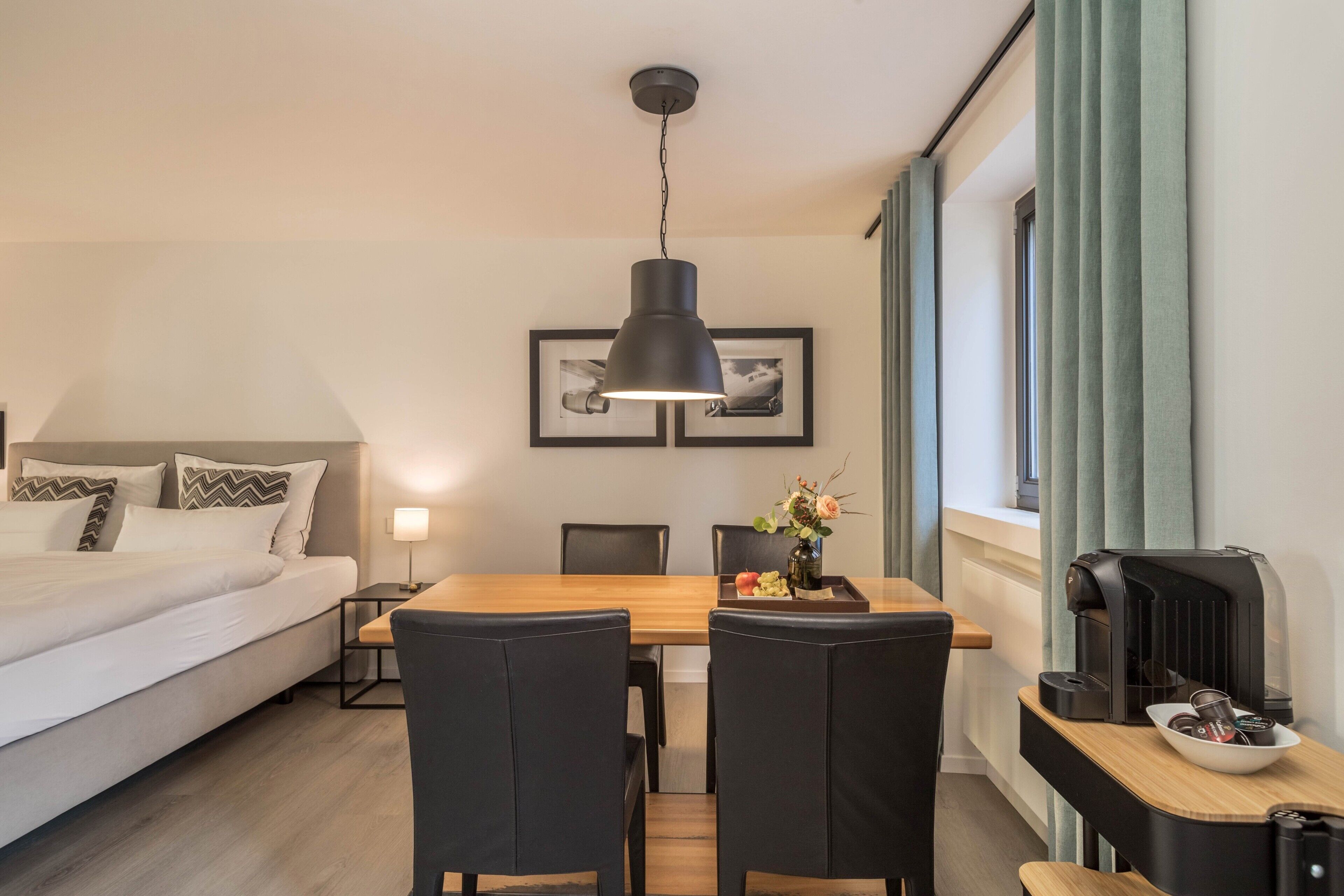 Ein Hotelzimmer mit Bett, Esstisch mit Stühlen, einer Kaffeemaschine und einem gerahmten Bild an der Wand.