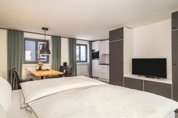A hotel room with a bed, a desk with a chair, a television, and a kitchenette. - Modern Studio Apartment No. 15 in the City Center with Wi-Fi (Wangen im Allgäu)