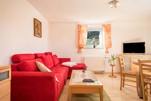 Ein Wohnzimmer mit einem roten Sofa, einem Holztisch, einem Fernseher und einem Fenster mit Vorhängen.