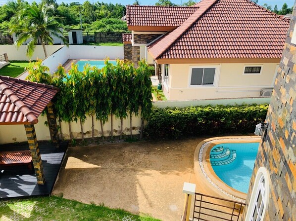 Zona residencial con piscina, tejado de baldosas y jardín con una palmera.