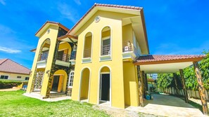 A two-story yellow house with a tiled roof, a balcony, and a covered porch.