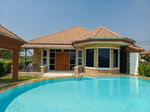 A residential property with a swimming pool, a covered patio, and a large wooden door.