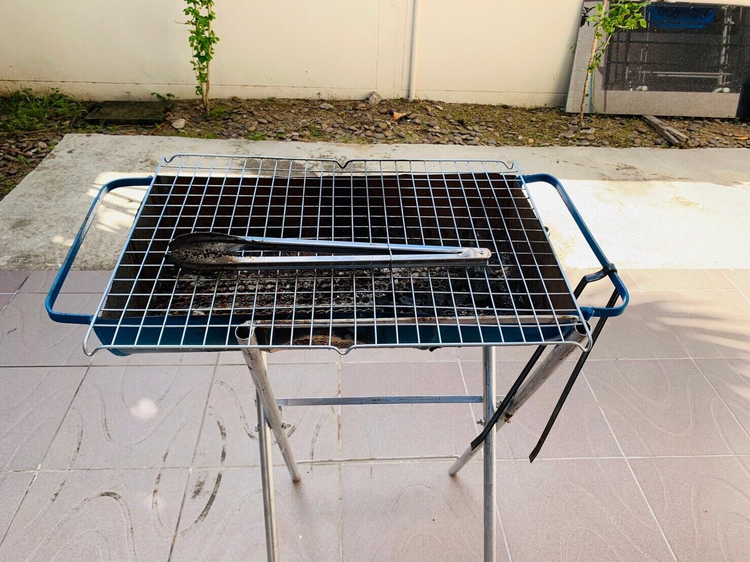 A portable grill with tongs on a tiled patio.