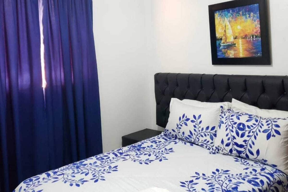 Ein Schlafzimmer mit Bett, Kopfstütze, Nachttisch, einem Gemälde und einem Deckenventilator.
