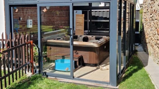 A glass-enclosed outdoor hot tub area with a wooden deck and a blue pool. - Neurazy by Interhome (Neurazy)