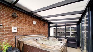 A hot tub area with a brick wall, wooden bench, and glass doors. - Neurazy by Interhome (Neurazy)