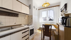 A compact kitchen with white cabinets, a stove, a sink, and a dining area with a chair and table. - Neurazy by Interhome (Neurazy)