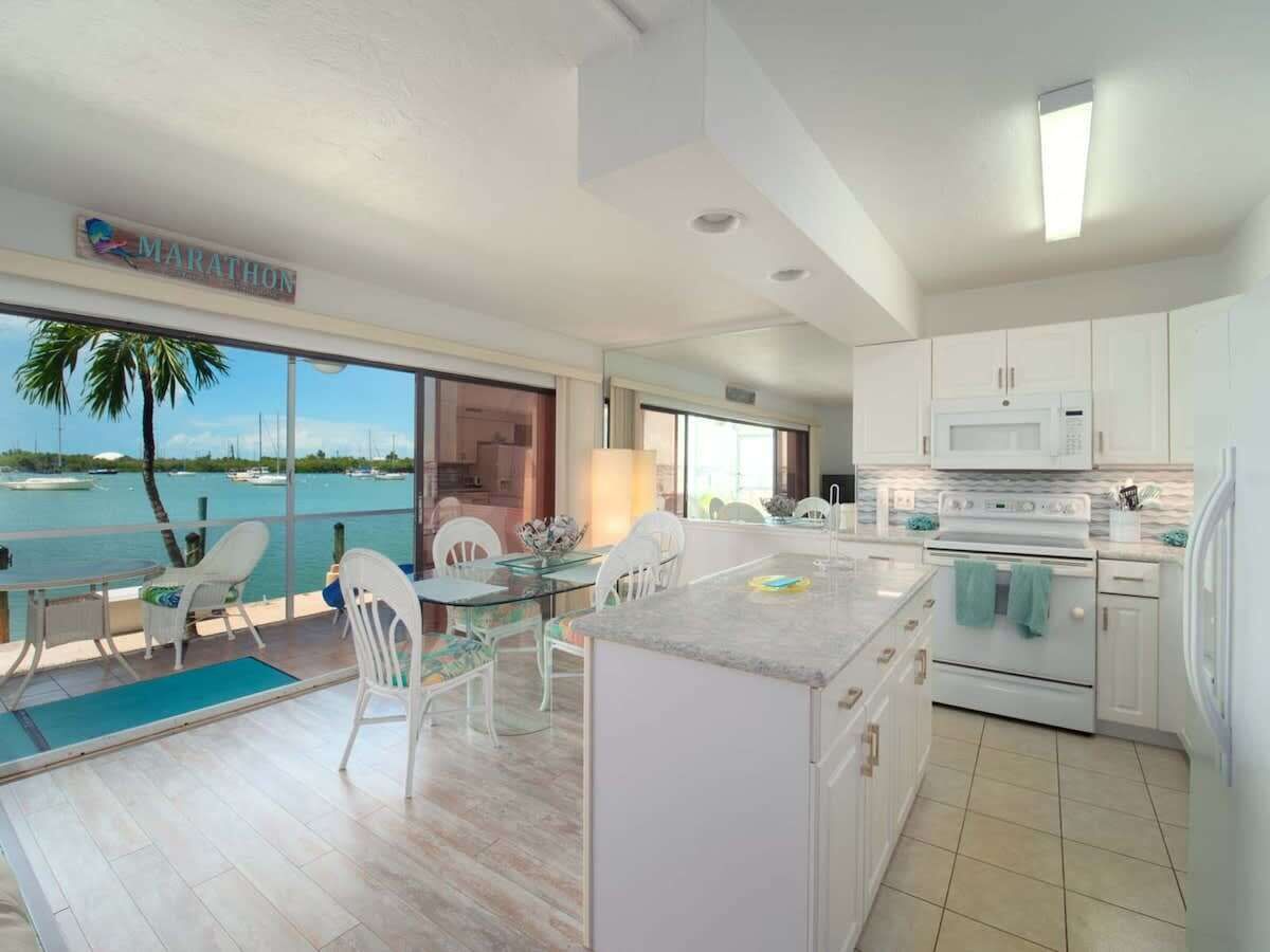 Een moderne keuken met witte kasten, een centraal eiland en uitzicht op de zee door grote ramen.