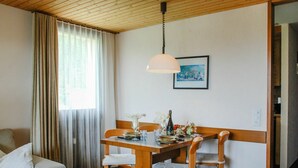 Et spiseområde med et træbord og stole, en hængende lampe, et maleri på væggen og et vindue med gardiner.