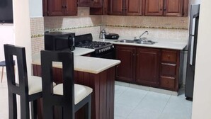 A compact kitchen with dark wooden cabinets, a built-in stove, a sink, and a small dining area with two chairs. - Residencial Las Dianas (Santiago de los Caballeros)