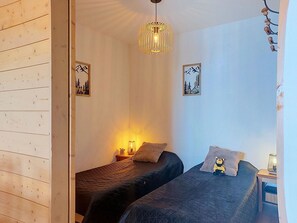 A room with two beds, a hanging light fixture, and two wall-mounted picture frames.